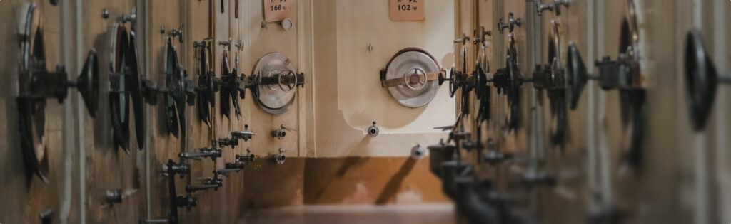 Row of metal fermentation tanks with round port holes in a heritage distillery