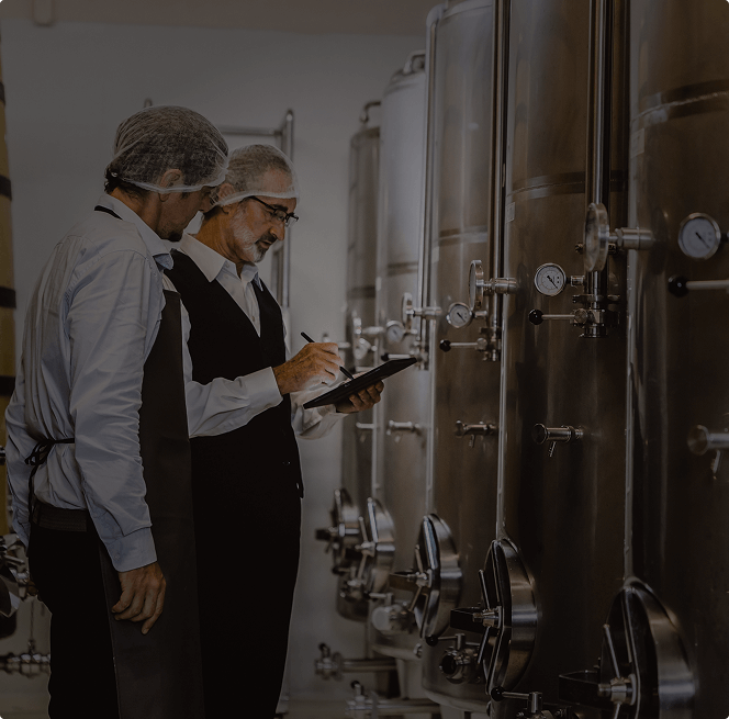 Two production specialists with a clipboard checking fermentation tanks with gauges