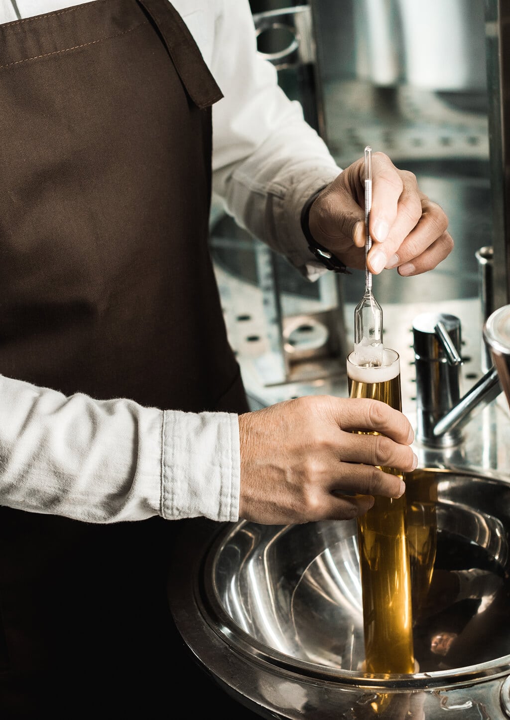 Brewer measuring alcohol content with a hydrometer in a cylinder of golden spirit
