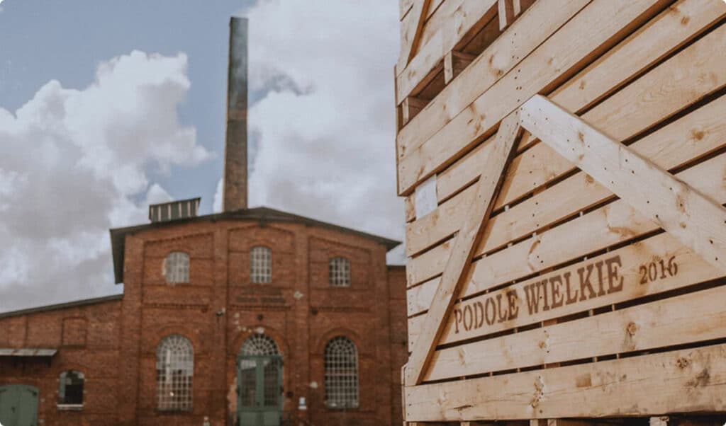 Historic distillery building with a brick chimney and a crate reading Podole Wielkie 2016