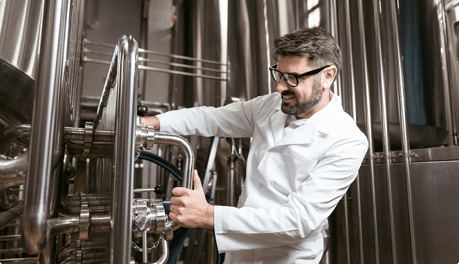 Lab-coated technologist operating a valve on a stainless steel tank in a production plant