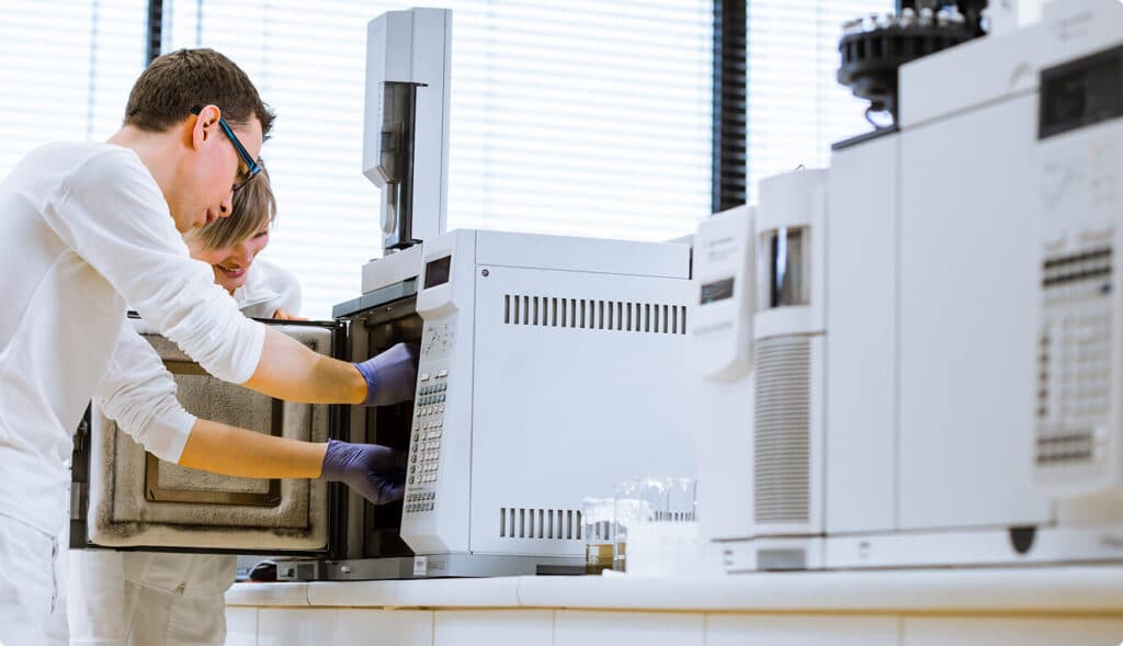 Two analysts at a gas chromatograph in a quality control laboratory