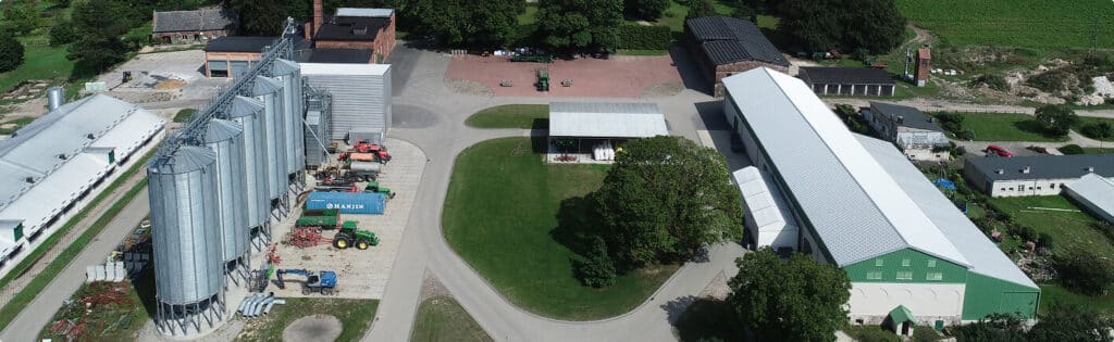Alquora site from a drone: silos, green tractors, white-roofed hall and brick building with chimney