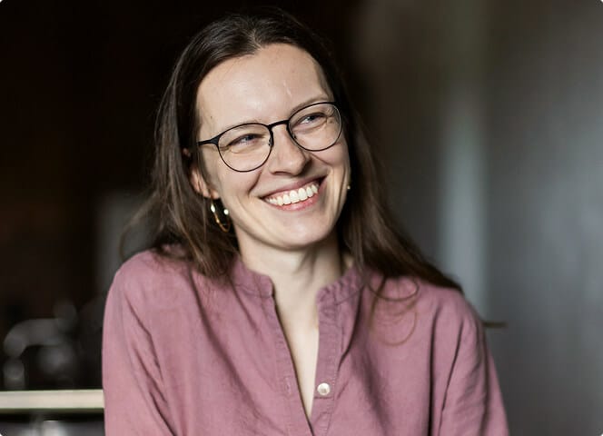 Smiling Alquora employee with glasses and a pink linen shirt, looking to the side