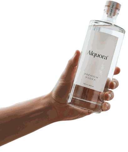 Hand holding a clear bottle of Alquora Premium vodka