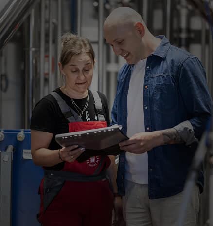 Woman in red overalls and man in denim shirt reviewing a folder at the Alquora distillery